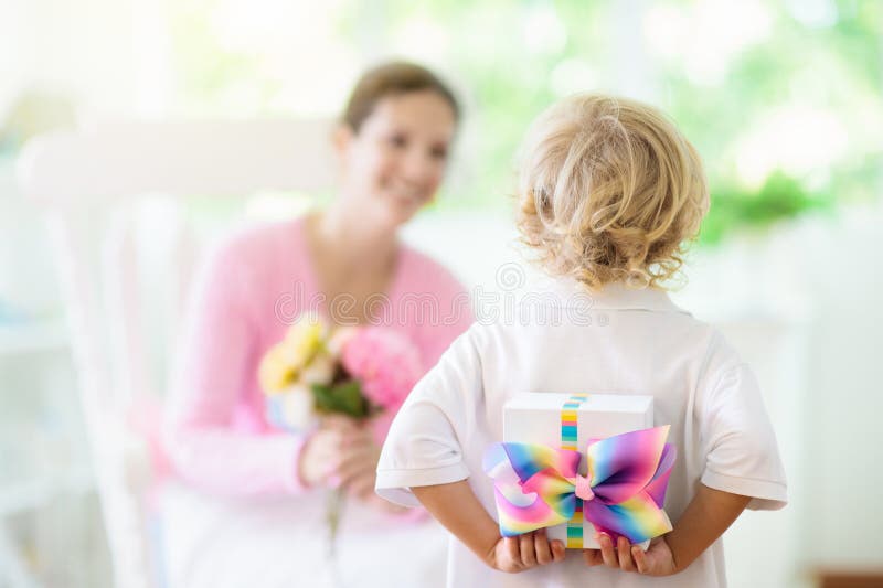 Happy Mothers Day. Child with present and flowers for mom. Little boy holding wrapped gift and flower bouquet for mother. Family celebrating spring holiday. Young women with small kid at home. Happy Mothers Day. Child with present and flowers for mom. Little boy holding wrapped gift and flower bouquet for mother. Family celebrating spring holiday. Young women with small kid at home